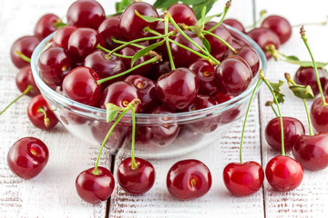 cherries with leaves in a bowl on a white wooden background