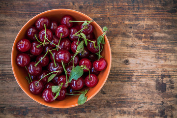 bowl of cherries with leaves on the old wooden background