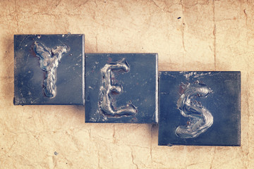 The word "YES" made from metal letters on an old vintage paper b
