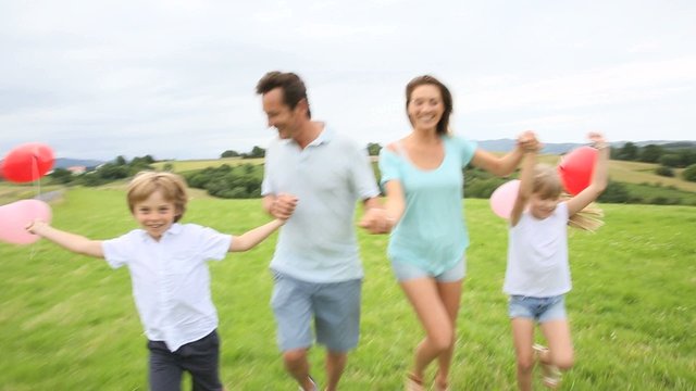Family running in countryside, kids holding balloons
