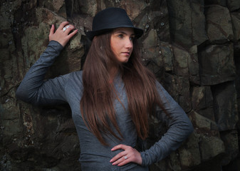 Beautiful young woman in black hat at the rock