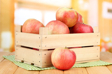 Ripe apples in wooden box, on bright background