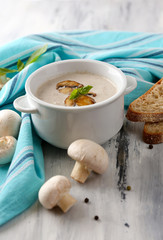 Mushroom soup in white pot, on napkin,  on wooden background