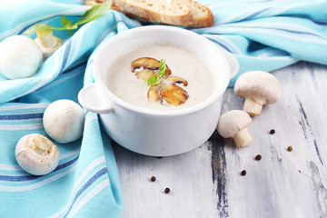 Mushroom soup in white pot, on napkin,  on wooden background