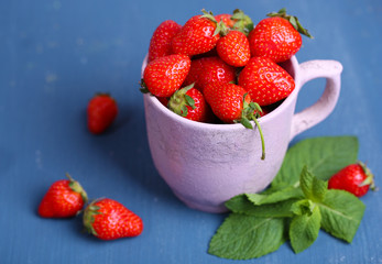 Ripe sweet strawberries in mug  on color wooden background