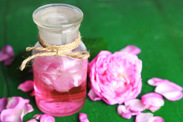 Rose oil in bottles on color wooden background
