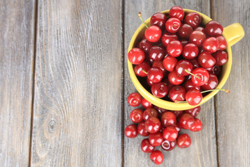 Sweet cherries in mug on wooden background