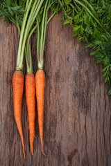 Bunch of fresh carrots with green leaves over wooden background