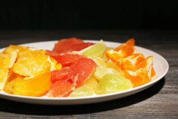 Sliced citrus fruits on plate, on wooden background