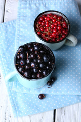 Summer berries in color mugs on color wooden background