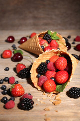 Different ripe berries in sugar cones, on wooden background