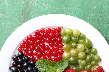 Forest berries on plate, on color wooden background