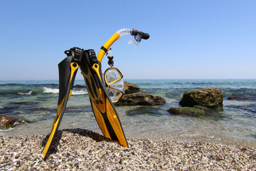 Flippers, mask and snorkel lying on sandy beach. Sea background