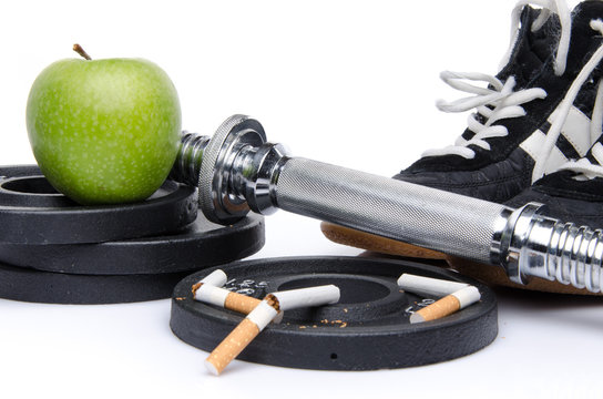 Dumbells, fitness shoes with an apple and broken cigarettes