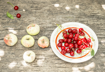 broken apples and a plate with cherries on old wooden table
