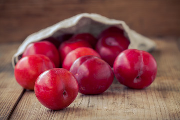 red plums in a bag on an old rustic wooden background