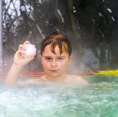 boy enjoys swimming in the warm outdoor pool with a snowball in