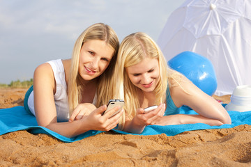 Zwei junge Frauen mit Mobiltelefon am Strand