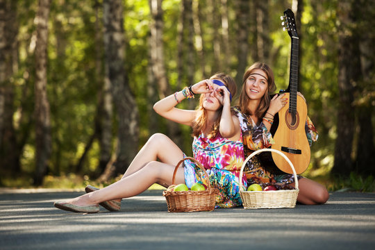Two hippie girls with guitar in a summer forest