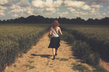 Young woman walking in a wheat field - obrazy, fototapety, plakaty