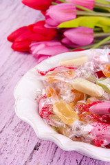Tasty candies in bowl with flowers on wooden background