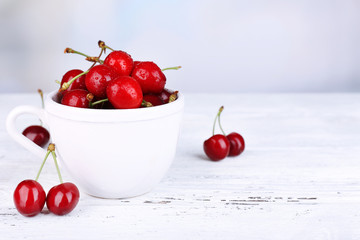 Ripe sweet cherries in cup on wooden table