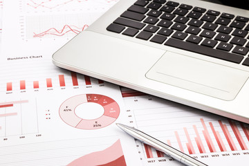 laptop and pen with red business charts, graphs, infomation and