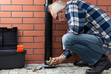 Husband cleaning pavement drain hole from autumn leaves
