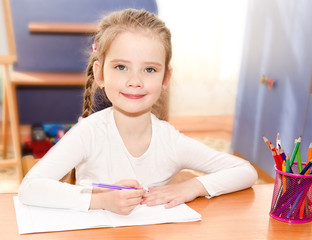 Cute smiling little girl is writing at the desk