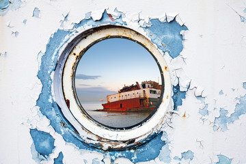 Ship wreck behind round porthole in white and blue wall