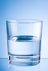 Half a glass of drinking water on blue background