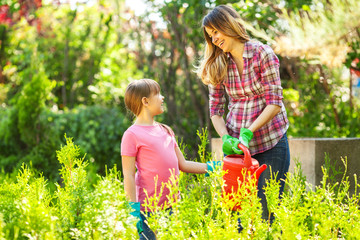 Mother And daughter watering plants in garden.