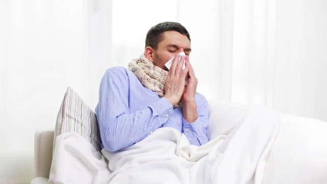 ill man with flu at home sneezing and blowing nose
