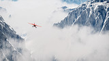 Red airplane flying over snow mountains in the clouds. Aerial sh