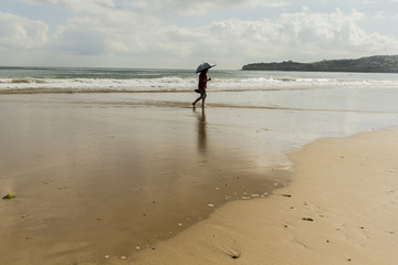 Hombre con paraguas paseando por la orilla de la playa