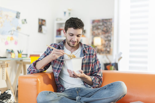 young man sitting on the couch eating Chinese noodles with chops