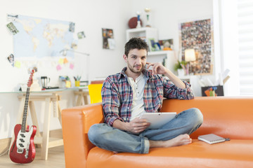 Fototapeta premium young man sitting on the couch and surfing on a digital tablet