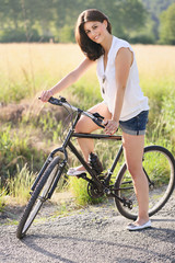 Smiling woman with bicycle on a country road