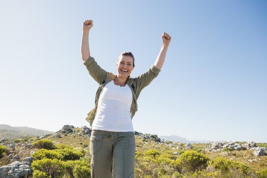 Pretty hiker cheering at camera on mountain terrain