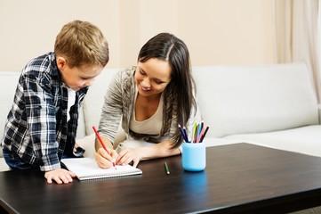 Happy young mother with her son drawing in home interior