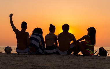 Silhouettes a young people sitting on a beach looking at  sunset