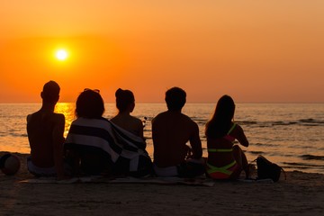 Silhouettes a young people sitting on a beach looking at  sunset