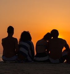 Silhouettes a young people sitting on a beach looking at  sunset