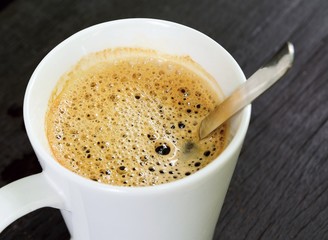 Top view to the white cup with brown coffee and spoon.