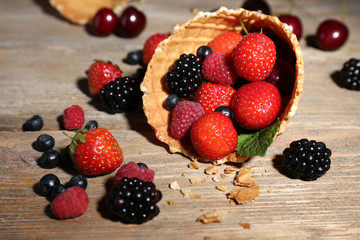 Different ripe berries in sugar cone, on wooden background