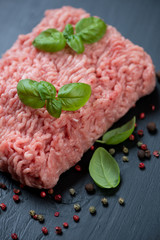Ground turkey meat with pepper and basil, black wooden surface