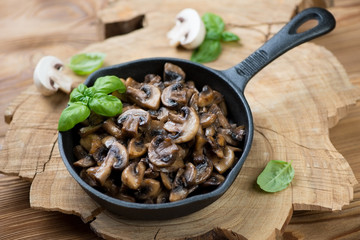 Roasted champignons in a frying pan over wooden background
