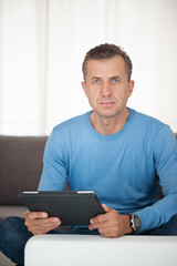 Fototapeta na wymiar Portrait of mature man relaxing at home in sofa with tablet