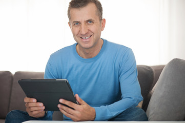 Portrait of mature man relaxing at home with tablet in sofa
