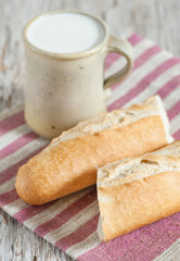 Baguette and milk in ceramic mug on the wooden board